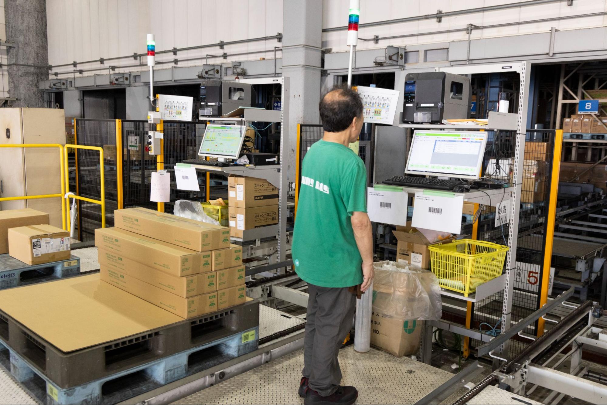 右：APTのシステムと連携する自動化設備により、出荷精度と作業効率を両立する物流現場。　左：キャプション：モニターで作業を確認する作業員。